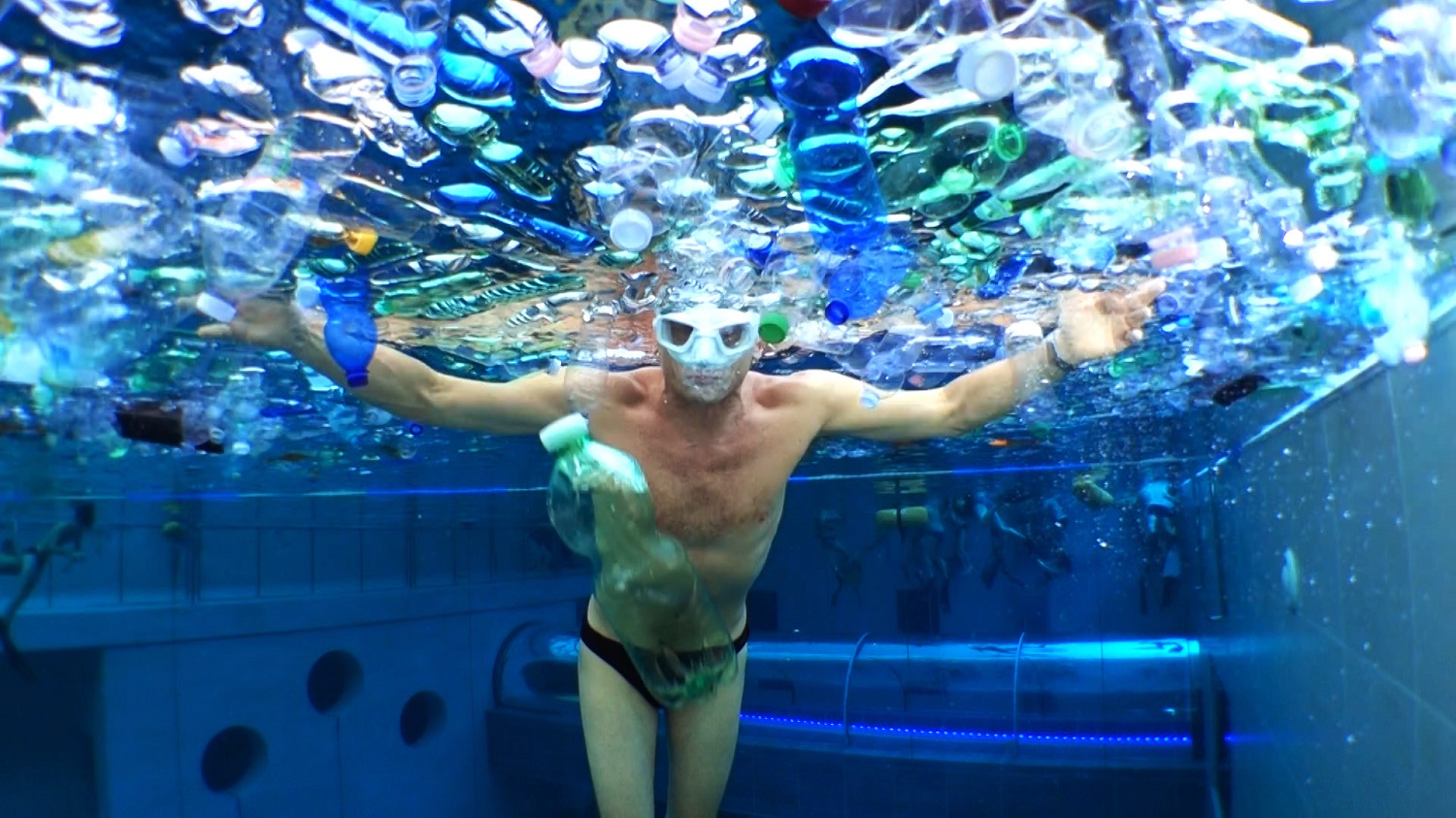 Uomo in piscina sommerso di bottiglie di plastica simula quello che accadrà al mare e a oceani se non cambiamo abitudini
